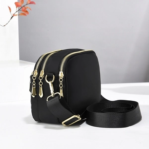 Detail view of the black crossbody bag with three golden zippers and wide fabric strap