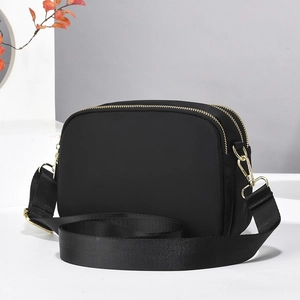 Detail of black crossbody bag featuring dual gold zippers and a wide nylon strap