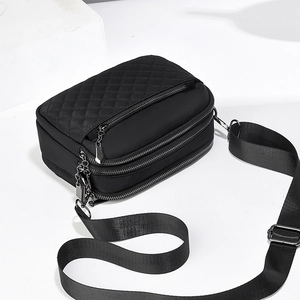 Detail of black quilted crossbody bag showing multi-layer zipper pockets and nylon texture