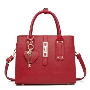 Detail of red leather handbag showing golden square lock and heart-shaped pendant detail