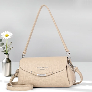 Elegant beige leather crossbody bag with metal trim shown in a minimalist studio setting