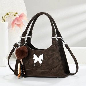 Sac à main marron mat avec papillon argenté et pompon sur support géométrique blanc