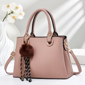 Detail of pink shoulder bag featuring herringbone texture, gold rings, and decorative fur charm