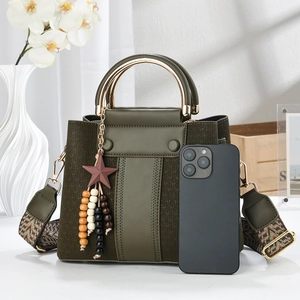 Detail of green leather handbag with gold handle and woven strap next to a smartphone