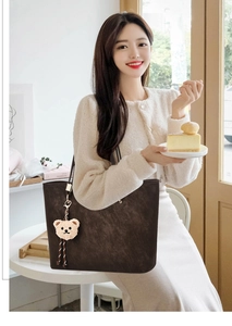 Close-up of dark brown leather tote bag with a white plush bear charm in a cafe