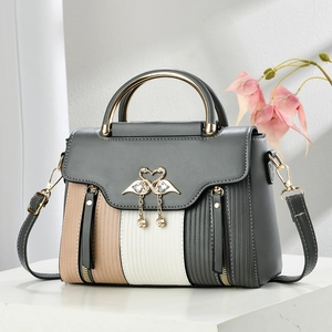 Detail of color-block PU leather bag with gold swan buckle and pearl charm on white pedestal