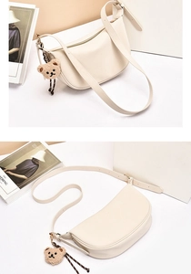 Detail view of beige crescent bag with smooth texture and cute brown plush bear charm