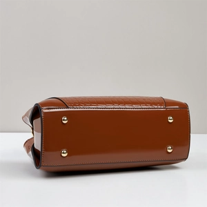 Detail view of brown glossy patent leather bag base with gold metal feet and croc pattern