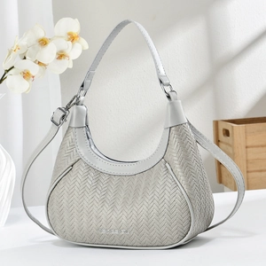 Light gray woven crescent handbag with metal logo and shoulder strap in minimalist setting