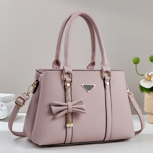 Détail d'un sac cabas en cuir rose clair avec pendentif nœud et finitions dorées