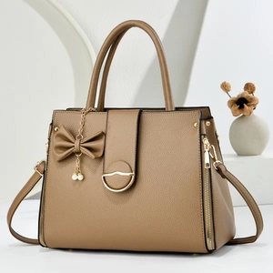 Detail of brown litchi pattern leather handbag with bow charm and gold side zippers