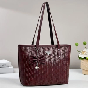 Detail of burgundy woven tote bag featuring silver logo and pearl bow charm accessory