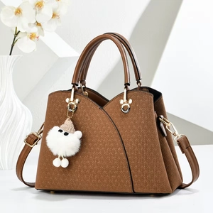 Detail of brown tote bag featuring woven texture and white plush pom-pom charm