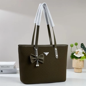 Detail of olive green woven tote bag featuring a pearl bow charm and metal triangle logo