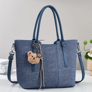 Blue woven tote bag with leather handles and a brown plush bear charm accessory
