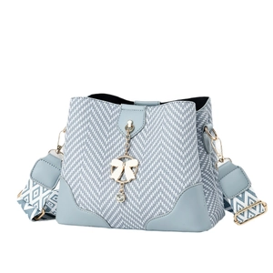 Light blue woven bucket bag with pearl bow charm and patterned wide shoulder strap