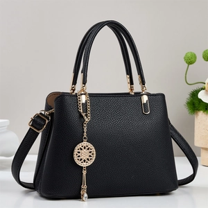 Detail of black pebbled leather tote with elegant gold metal pendant and sturdy handles