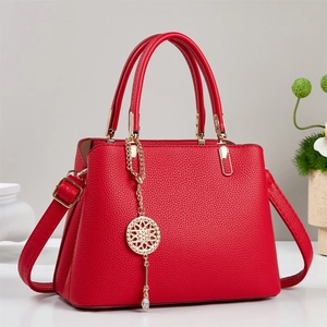 Detail of red lychee leather handbag featuring golden hardware and decorative round pendant