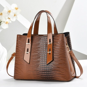 Detail of crocodile embossed tote bag with glossy dark brown texture and gold hardware