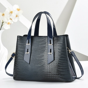 Dark blue crocodile pattern tote bag with dual handles and gold hardware on white pedestal
