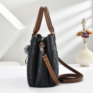 Detail of black textured tote bag with brown leather handles and plush charm accessory