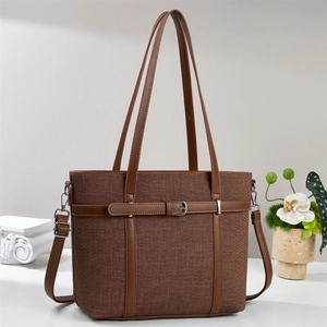 Brown canvas tote bag with leather trim and shoulder strap on minimal studio background