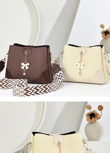 Detail view of bucket bag showing textured patchwork, golden bow charm and wide woven strap