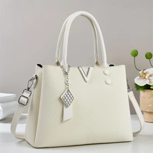 Detail of cream macaron tote bag with silver V-hardware and quilted square pendant charm