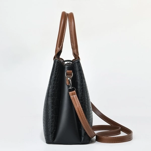Detail of black crocodile texture handbag with brown handles and silver metal hardware