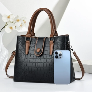 Detail of crossbody bag with crocodile texture and leather strap next to smartphone