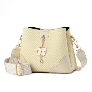 Pale yellow woven bucket bag with cream leather trim and a golden bow pendant