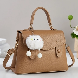 Detail of camel lychee textured leather handbag with plush monster charm and top handle
