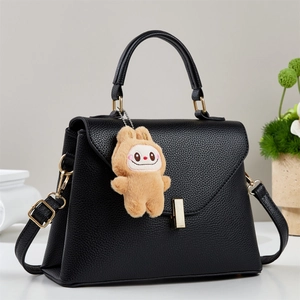 Dettaglio borsa in pelle nera con chiusura dorata e ciondolo di peluche marrone