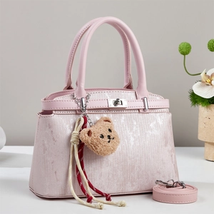 Detail view of pink textured handbag with plush bear charm and silver twist lock