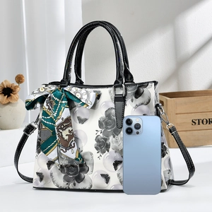 Détail d'un sac à main vintage fleuri avec foulard, incluant un smartphone pour l'échelle