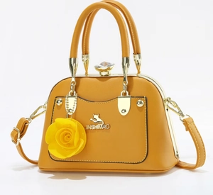 Detail of yellow tote bag with golden cat logo and decorative 3D rose charm attachment