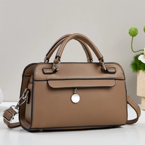 Sac bandoulière en cuir marron avec breloque argentée et bandoulière sur table blanche