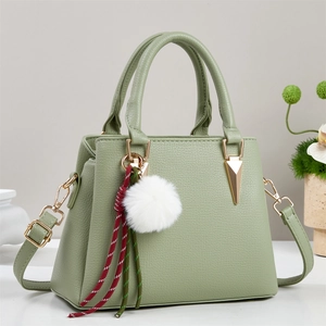 Detail of lychee pattern leather handbag in sage green with golden hardware and pompom decor