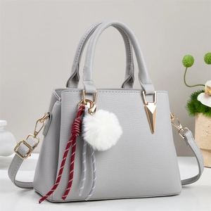 Close-up of light gray pebbled leather handbag with plush ball and woven strap detail