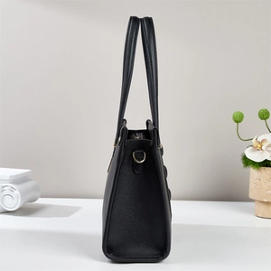 Side view of black lychee grain leather tote bag with gold D-ring and elegant orchid decor