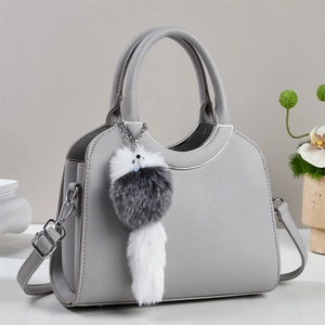 Détail du sac seau gris avec bordure métallique, cuir grainé et accessoire en peluche