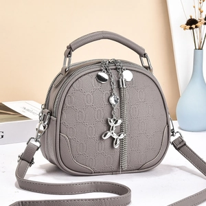 Detail of round grey crossbody bag featuring floral embossing and metal balloon dog charm