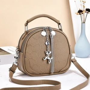 Detail of a brown textured leather round bag with dual zippers and silver charms