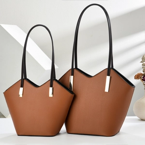 Brown leather tote bag set with V-shaped opening and black handles in soft window light