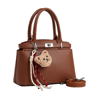 Brown litchi grain leather handbag with top handle and plush bear charm on white background
