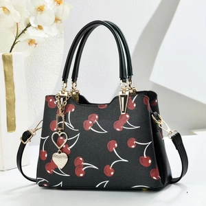 Elegant black leather handbag with red cherry print and heart charm in a studio setting
