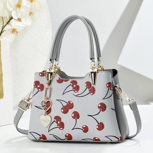 Detail of grey handbag with cherry print, cross-grain texture and heart pendant