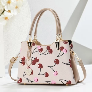 Detail of elegant handbag with cherry print, golden metal hardware and heart pendant