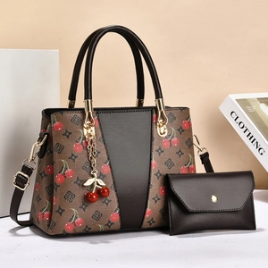 Detailed view of tote bag and envelope pouch set with cherry print and gold hardware