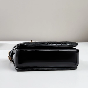 Detail of black glossy patent leather shoulder bag with embossed crocodile texture and gold hardware
